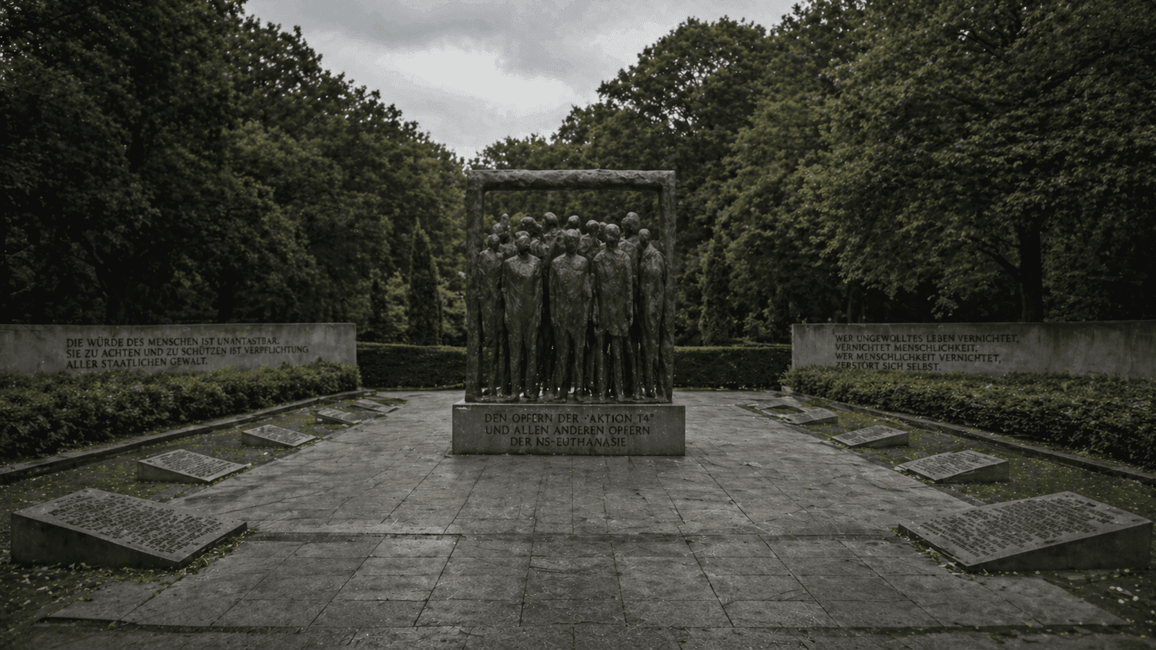 A solemn memorial garden with stone markers and a central commemorative sculpture in a European setting