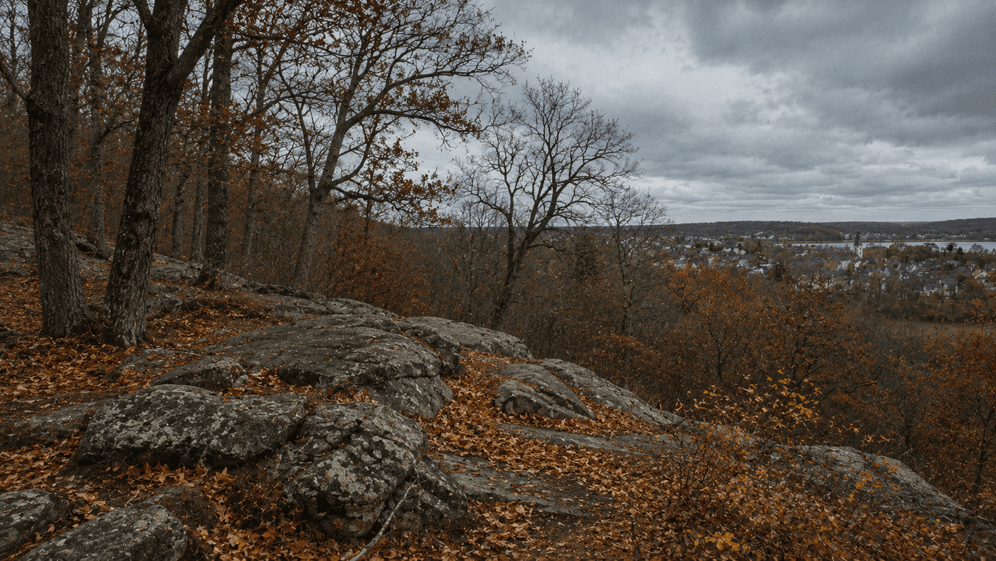 A rocky tree-covered hillside in Salem Massachusetts in autumn with colonial-era wooden buildings visible in the distance